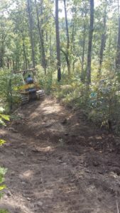 Eroding forest trail being rehabilitated with shaping and water bar installation.
